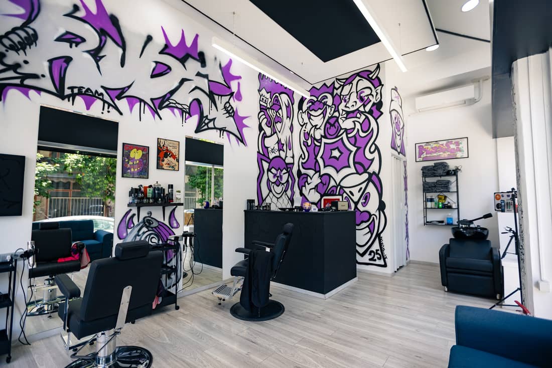 Το εσωτερικό του RUDE BARBERSHOP τη μέρα: ο μωβ γκράφιτι τοίχος, οι μαύρες καρέκλες και ο μπλε καναπές